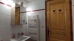 A bathroom with a white sink, mirror, and towel rack. There is a wooden door with two heart-shaped handles.