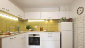 Een kleine keuken met witte kastjes, een ingebouwde oven, een spoelbak en een koelkast.