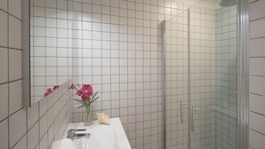 Een moderne badkamer met witte tegels, een witte wastafel, een douchecabine met glazen wanden en een spiegel boven de wastafel.