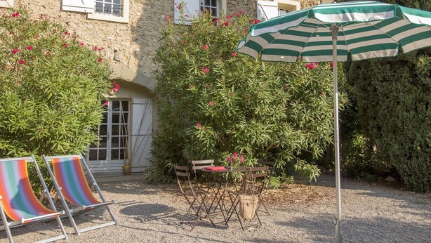 Een terras met twee gestreepte parasols, een tafel en twee stoelen.