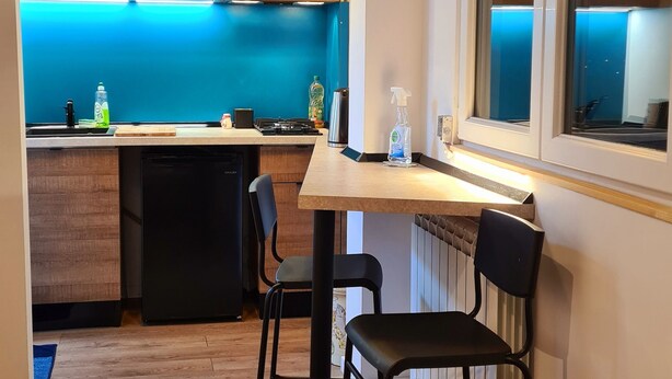 A modern kitchen with wooden cabinets, a dining area with two black chairs, and a large window with blinds. - Studio with Lake View (București)