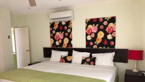 A hotel room with a bed, a nightstand, a red lamp, and floral wall art. - 1 Bedroom Penthouse Suite 63, Mystic Ridge Resort (Ocho Rios)