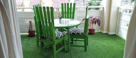 A green outdoor seating area with a round table and chairs, potted plants, and a welcome mat.