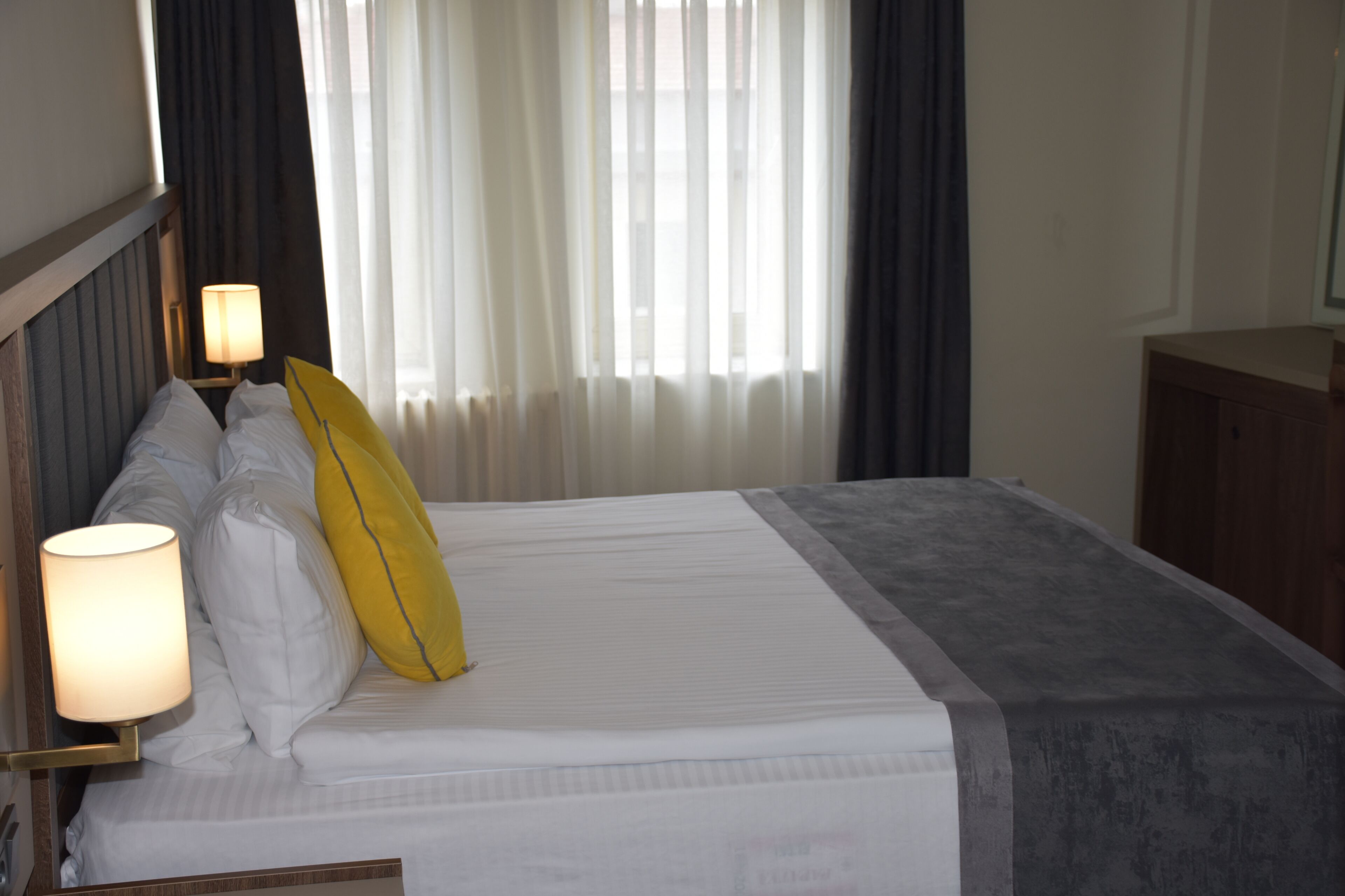 Een hotelkamer met een bed, een bedlamp, een nachtkastje en een raam met gordijnen.