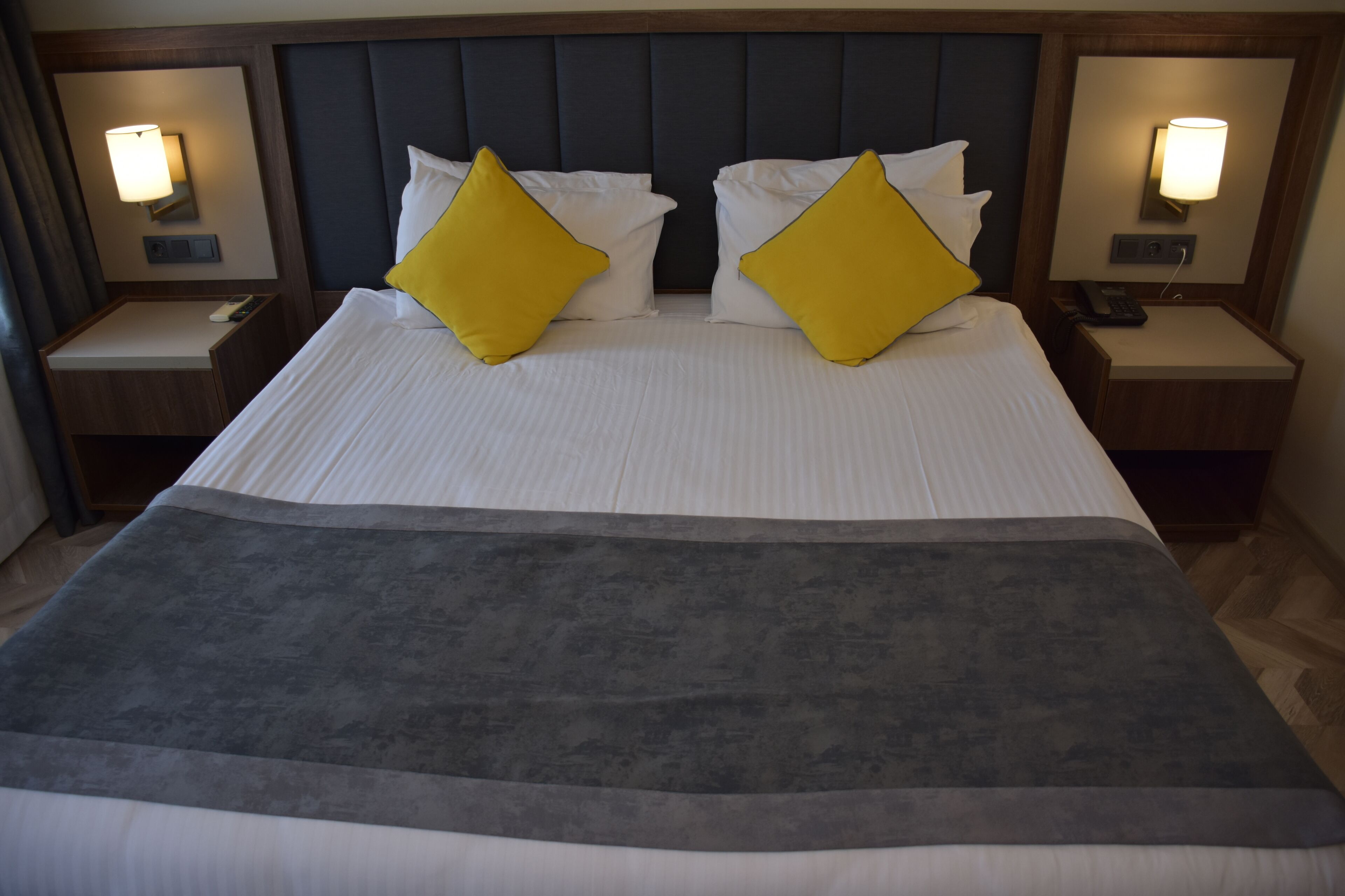 A hotel room with a large bed, two bedside tables, a nightstand, and a headboard.
