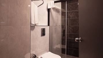 Un baño moderno con inodoro, cabina de ducha con mampara de cristal y barra para toallas.