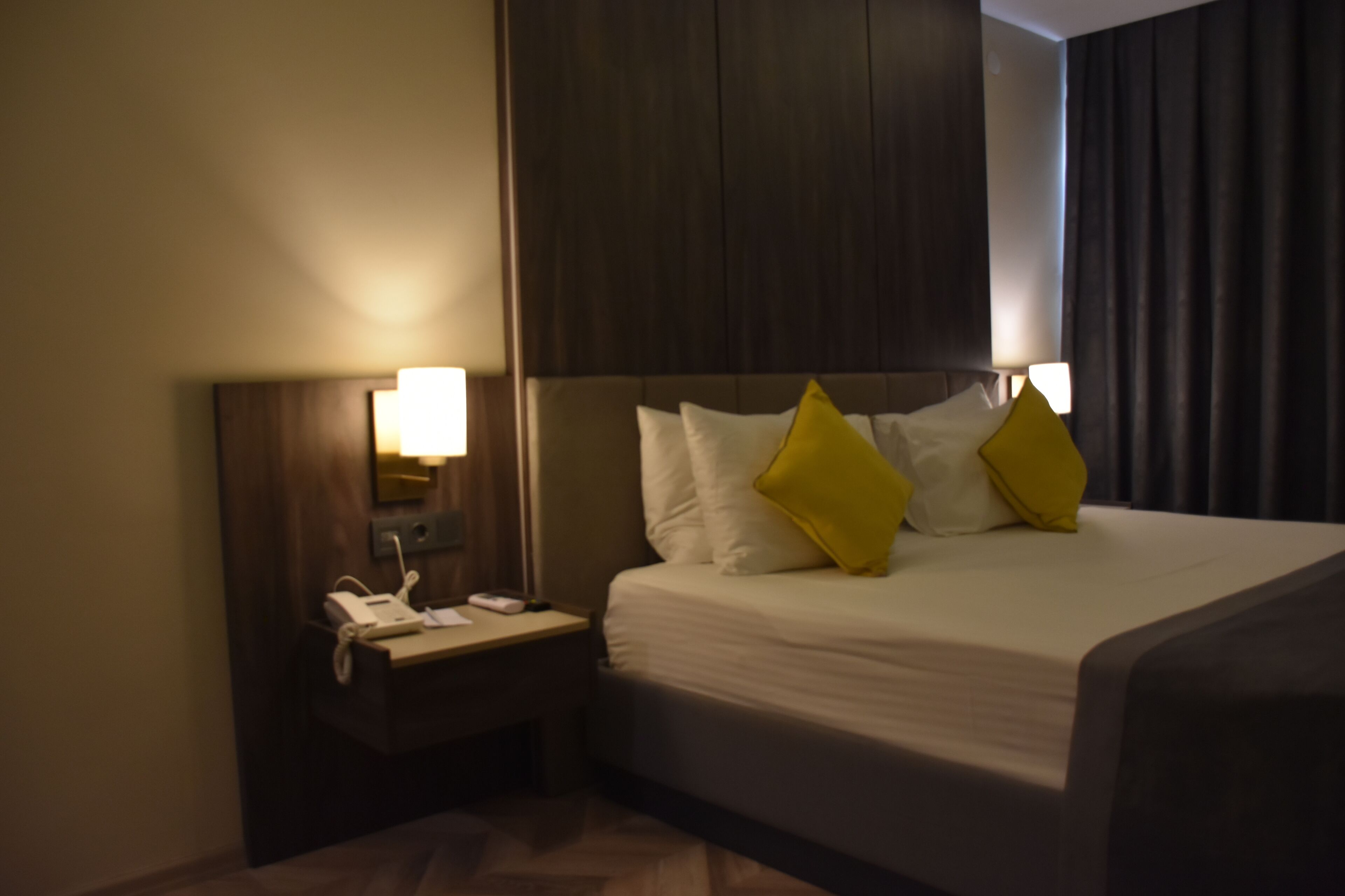 Une chambre d’hôtel avec un lit, une table de chevet, une lampe et une tête de lit sombre.