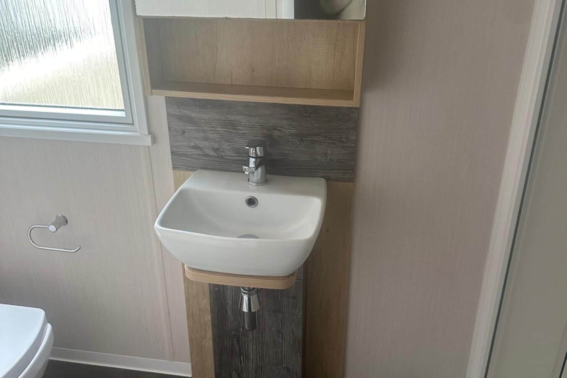 Ein Badezimmer mit einem weißen Waschbecken, einem Holz-Waschtisch und einem Fenster.