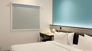 Ein modernes Hotelzimmer mit einem großen Bett, einem Schreibtisch mit Stuhl und einem an der Wand montierten Projektor.