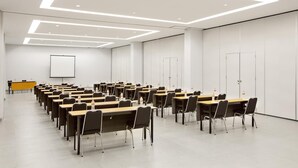 Ein Konferenzraum mit mehreren Tischen und Stühlen, einer Projektionsleinwand und einem Präsentationstisch.