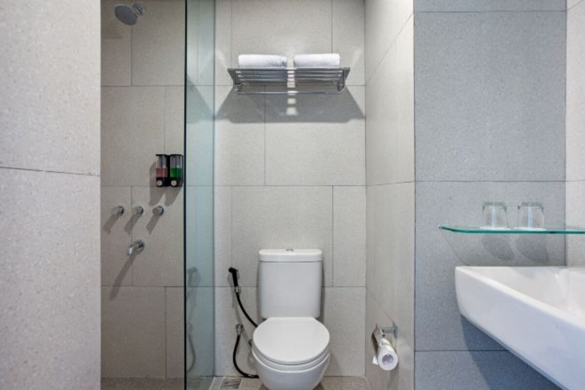 A modern bathroom with a glass shower enclosure, a white toilet, and a glass shelf above the toilet.