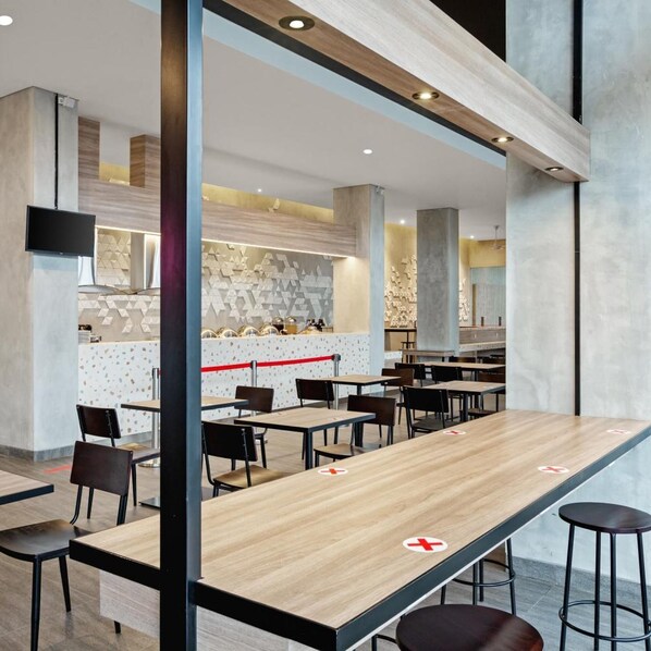 A modern restaurant with long tables, chairs, and a counter area. - Amaris Hotel Tasikmalaya (Tasikmalaya)