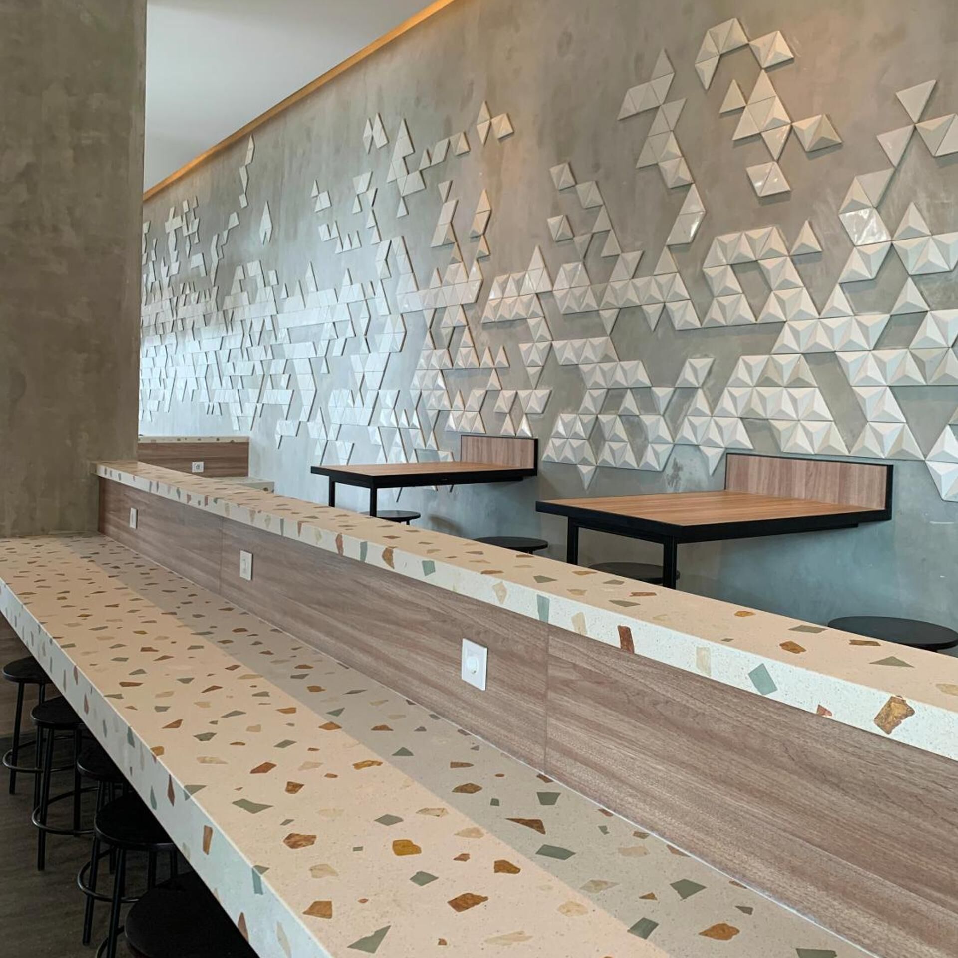 A modern bar area with a long counter, two tables, and a geometric wall design.
