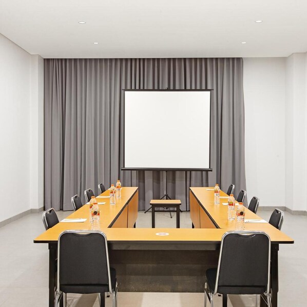 Un salón de conferencias con una larga mesa, sillas, una pantalla de proyector y un telón de fondo.