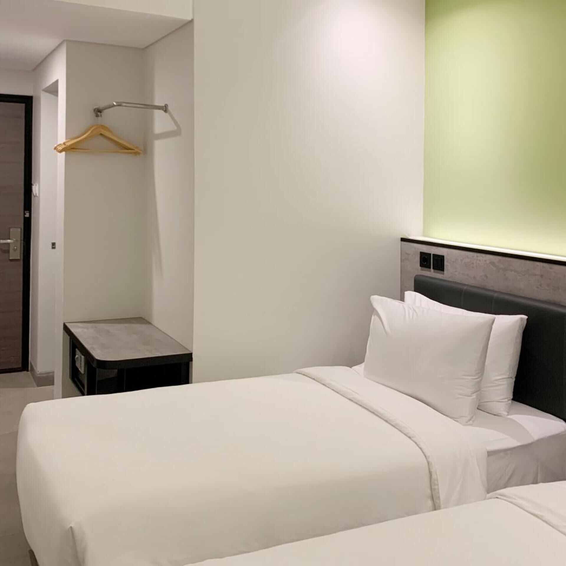 Une chambre d’hôtel avec un lit, une table de chevet, un porte-manteau mural et un mur d’accent vert.