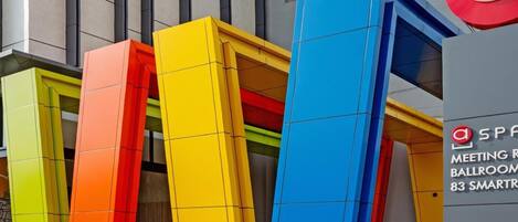 Un bâtiment moderne doté de panneaux verticaux aux couleurs vives, ainsi que d’une enseigne indiquant l’emplacement d’une salle de réunion et d’un salon de réception.