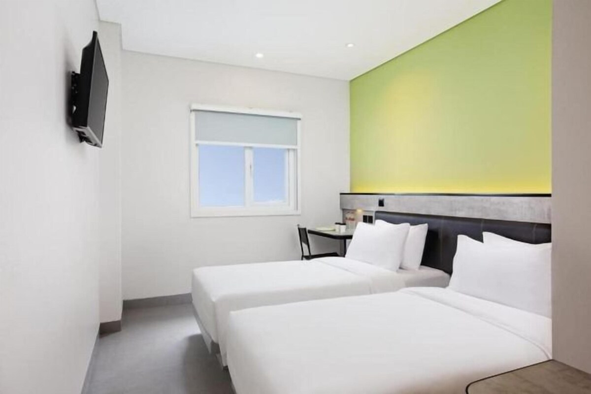 Une chambre d’hôtel avec deux lits, un téléviseur fixé au mur, une fenêtre et un mur d’accent de couleur verte.