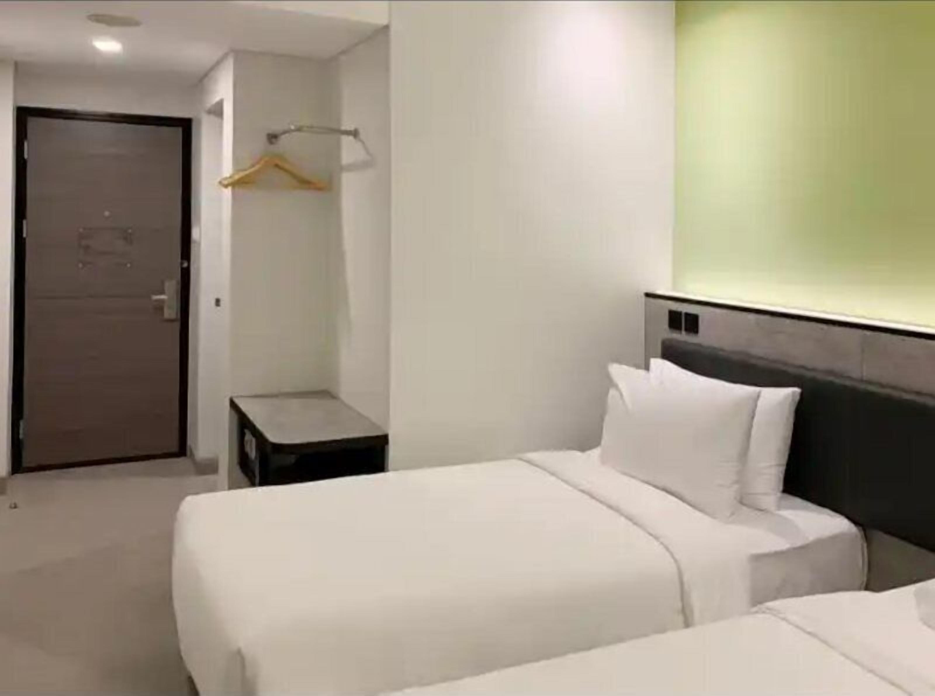 Una habitación de hotel con una cama, una mesita de noche, un perchero y una puerta.