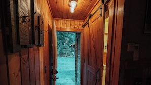 Un estrecho pasillo de madera con una puerta que da al exterior, una lámpara en el techo y un refrigerador a la derecha.