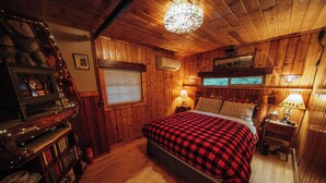Una habitación acogedora de madera con una cama, una chimenea, una estantería y una ventana.
