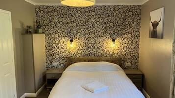 Une chambre à coucher comprenant un lit, deux tables de chevet, une commode, un luminaire fixé au mur et un plafonnier.