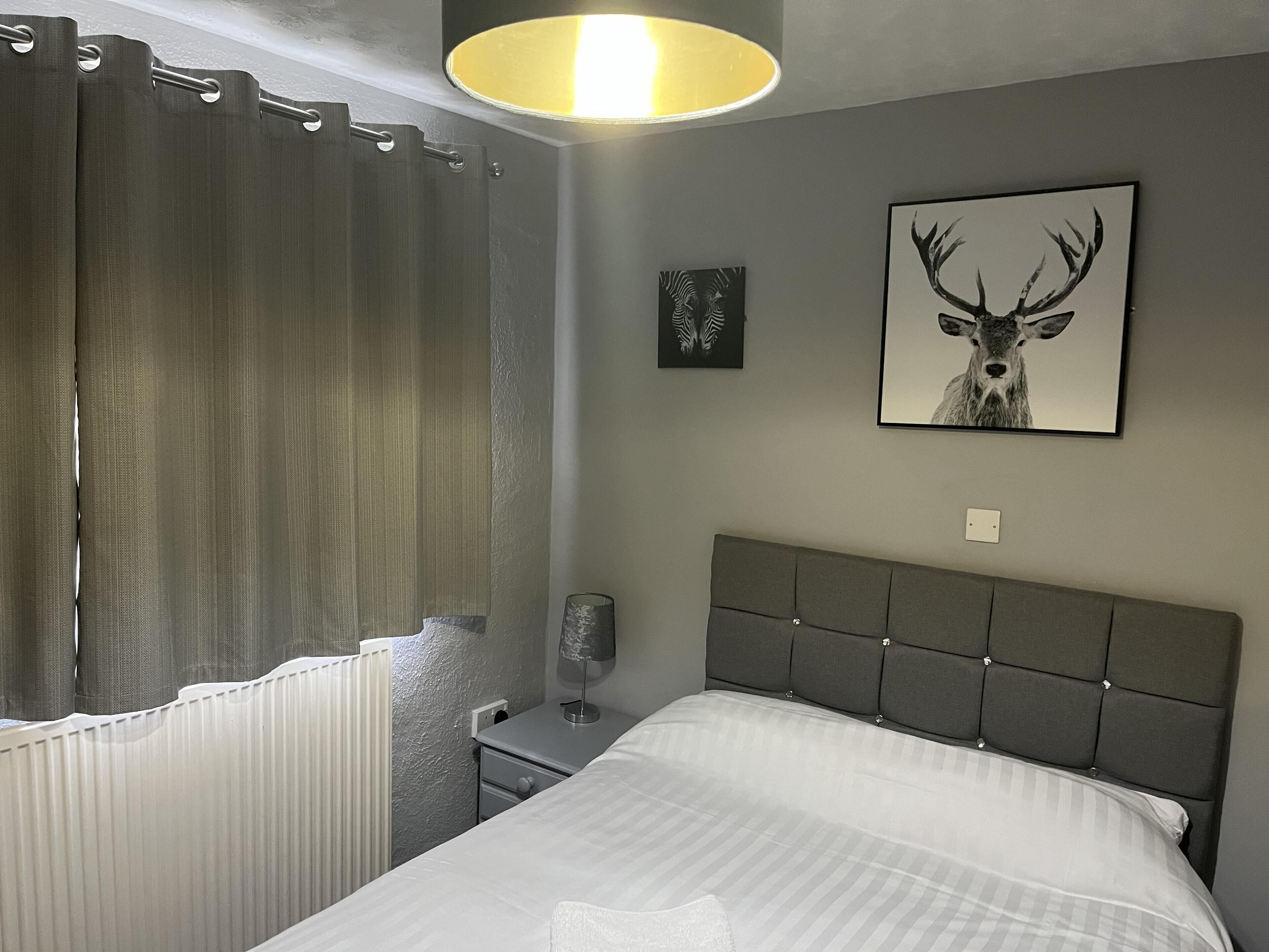 Une chambre à coucher comprenant un lit, une table de chevet, une lampe, un radiateur et une fenêtre avec des rideaux.