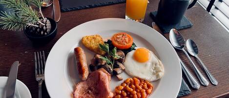 A breakfast plate with eggs, sausages, mushrooms, beans, and a tomato on a wooden table.