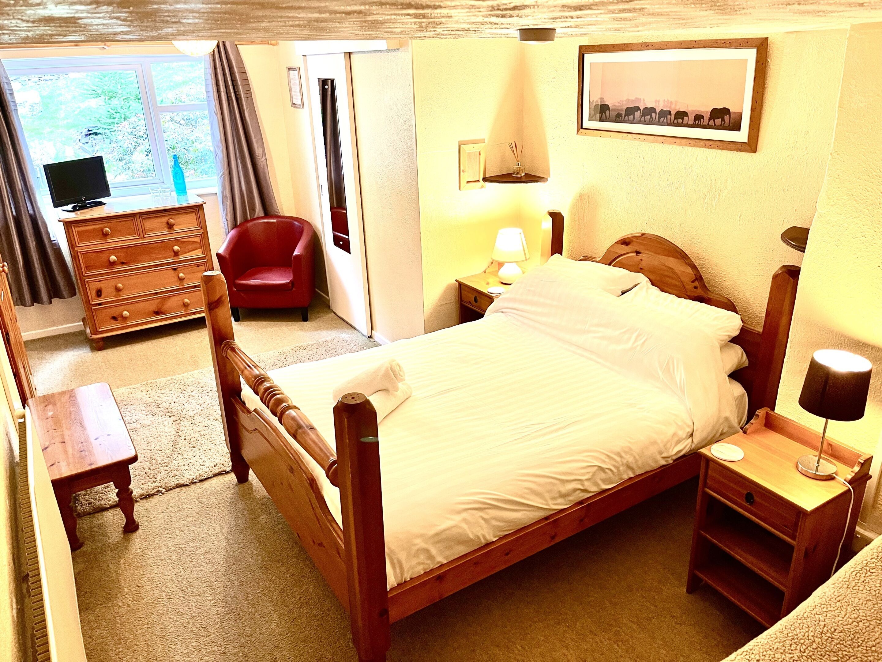 Un dormitorio con una cama de madera, un aparador, una silla, una mesita de noche con lámpara y una ventana con cortinas.