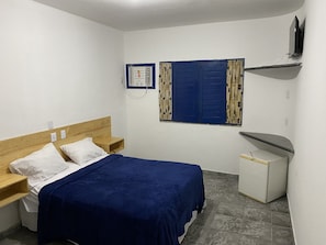 A small, clean room with a single bed, a nightstand, a dresser, a window with curtains, and a TV mounted on the wall. - Pousada Villa Grécia (Aracaju)