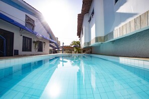 A swimming pool with clear blue tiles, surrounded by buildings with white walls and blue accents. - Pousada Villa Grécia (Aracaju)