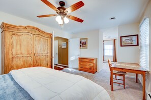 A bedroom with a wooden wardrobe, a bed with a white duvet, a wooden dresser, a dining table with a chair, and a ceiling fan. - Big Country Home (Harpers Ferry)