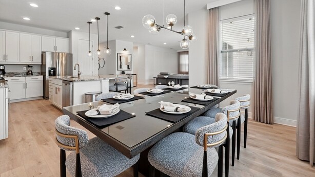 Une cuisine moderne avec des meubles blancs, un réfrigérateur en acier inoxydable et un coin repas comprenant une longue table et six chaises.