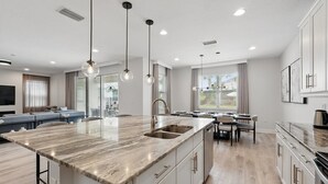 Une cuisine moderne dotée d’un grand îlot central, de luminaires suspendus et d’un coin repas avec une table et des chaises.