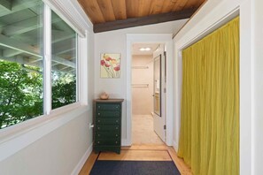 Un couloir avec un plafond en bois, une fenêtre donnant sur des arbres, une commode verte et un rideau jaune.