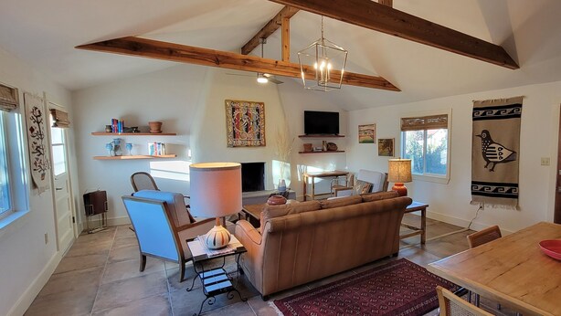 A spacious living room with a sofa, dining table, and a fireplace. There are shelves with books and decorative items, and a television mounted on the wall. - Luxury Adobe Home near Marfa and McDonald Observatory (Fort Davis)