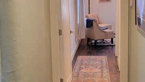 A hallway with a patterned rug, a chair, and a painting on the wall. - Luxury Adobe Home near Marfa and McDonald Observatory (Fort Davis)