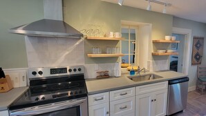 A modern kitchen with stainless steel appliances, wooden shelves, and a dishwasher. - Luxury Adobe Home near Marfa and McDonald Observatory (Fort Davis)