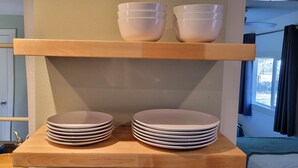 A stack of white plates and bowls on a wooden table in a room with a window and a door in the background. - Luxury Adobe Home near Marfa and McDonald Observatory (Fort Davis)