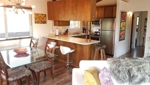 Eine moderne Küche mit Holzausstattung, einer zentralen Kochinsel, Edelstahlgeräten und einem Essbereich mit Glastischen und Stühlen.