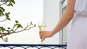 Un balcon avec un présentoir à plusieurs niveaux rempli de pâtisseries et un verre de vin blanc.