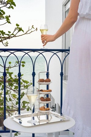 A balcony with a tiered tray of pastries and a glass of white wine.