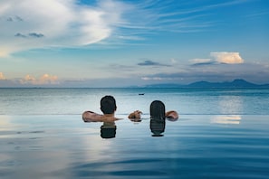 A couple relaxing on an infinity pool with a view of the sea and distant mountains.