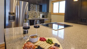 Una cocina con encimera de mármol, refrigerador de acero inoxidable y una mesa de desayuno con carnes, quesos, frutas y una copa de vino.