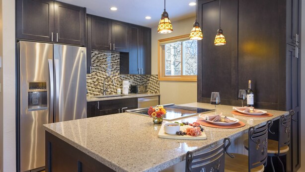 Una cocina moderna con gabinetes oscuros, electrodomésticos de acero inoxidable, encimera de granito e iluminación colgante.