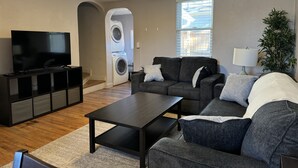Een woonkamer met een flatscreen televisie, een zithoek, een salontafel en een wasmachine op de achtergrond.