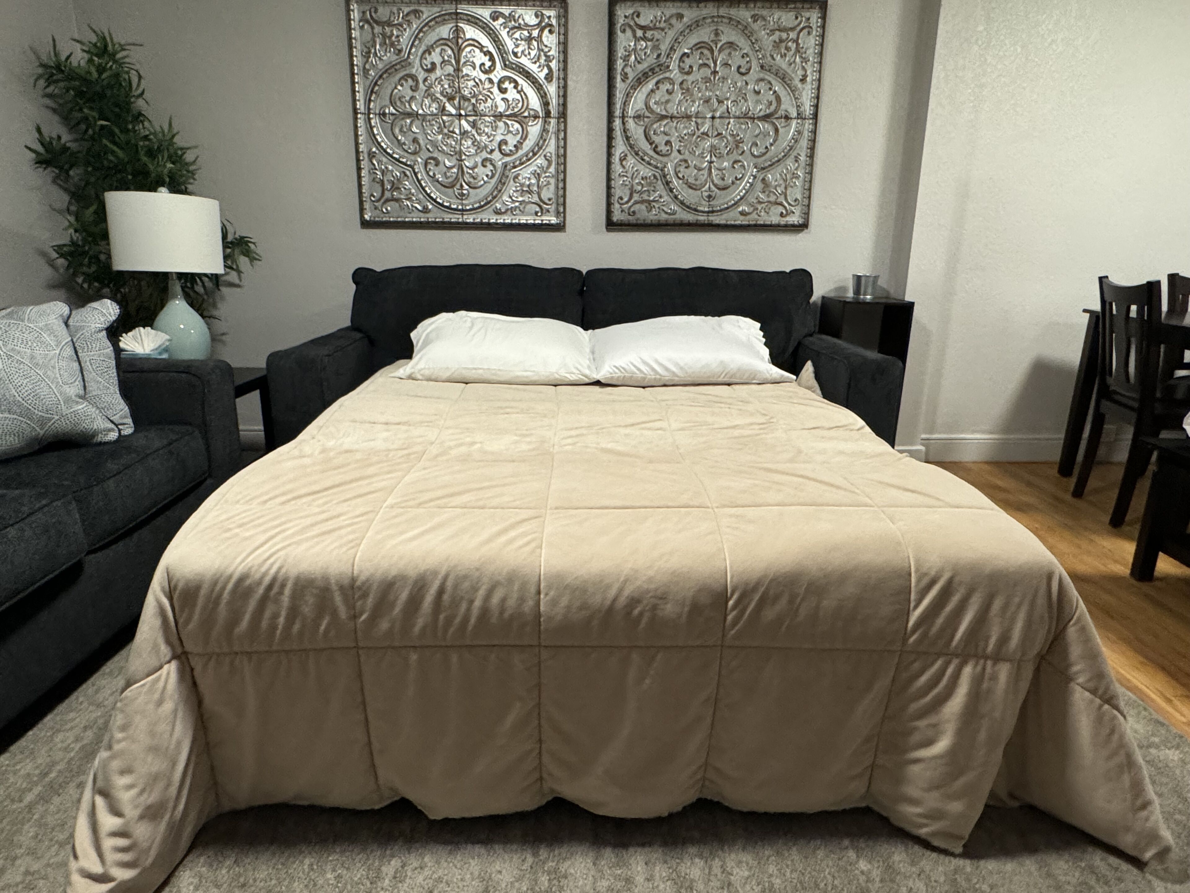 A bedroom with a large bed, a dark-colored sofa, a small table, and two decorative wall pieces.