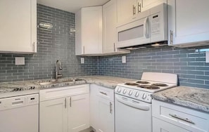 Una cucina con mobili bianchi, un forno a microonde, un piano cottura e una lavastoviglie.