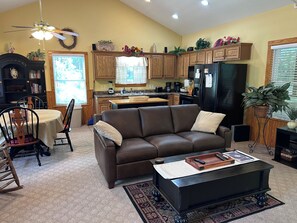 A living room with a brown leather sofa, a coffee table, and a dining area with a wooden table and chairs.