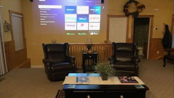 A living room with two leather chairs, a coffee table with books and a plant, and a large screen displaying a streaming service interface.