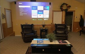Ein Wohnzimmer mit zwei Ledersesseln, einem Couchtisch mit Büchern und einer Pflanze, und einem großen Bildschirm, der eine Streaming-Dienstanwendung anzeigt.